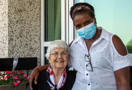 a geriatric care worker stands next to an elderly woman.